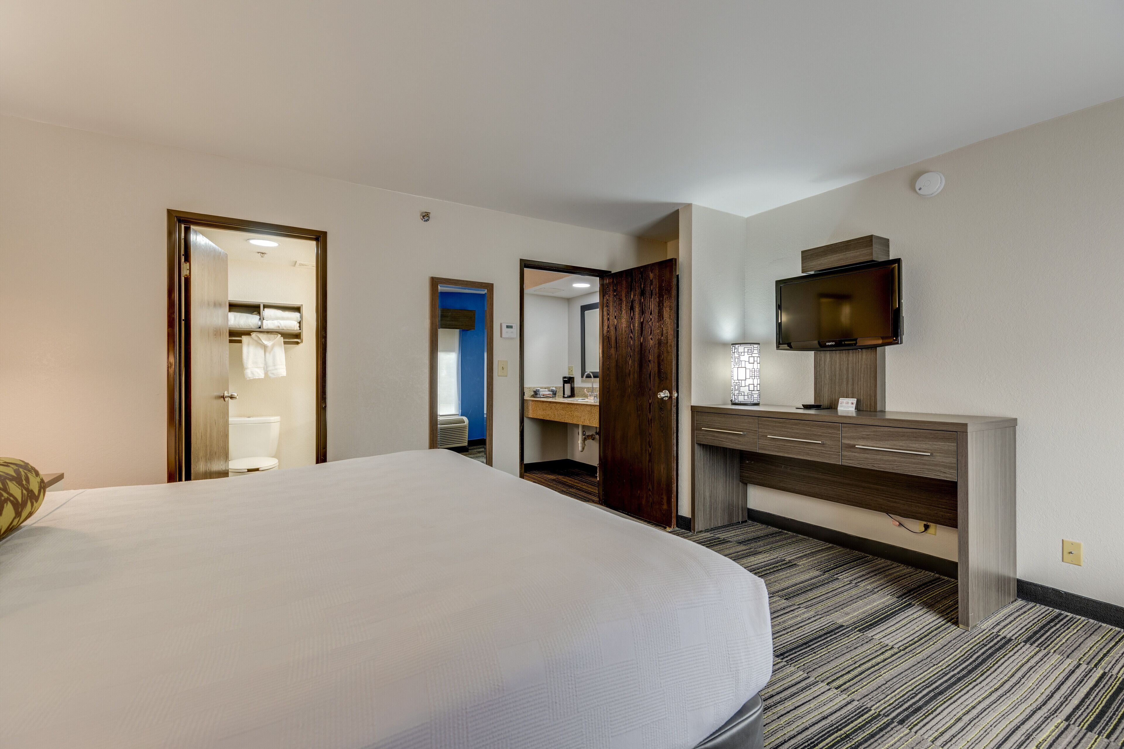 Une chambre d’hôtel avec un grand lit, une commode en bois, une télévision et une salle de bain visible à travers une porte ouverte.