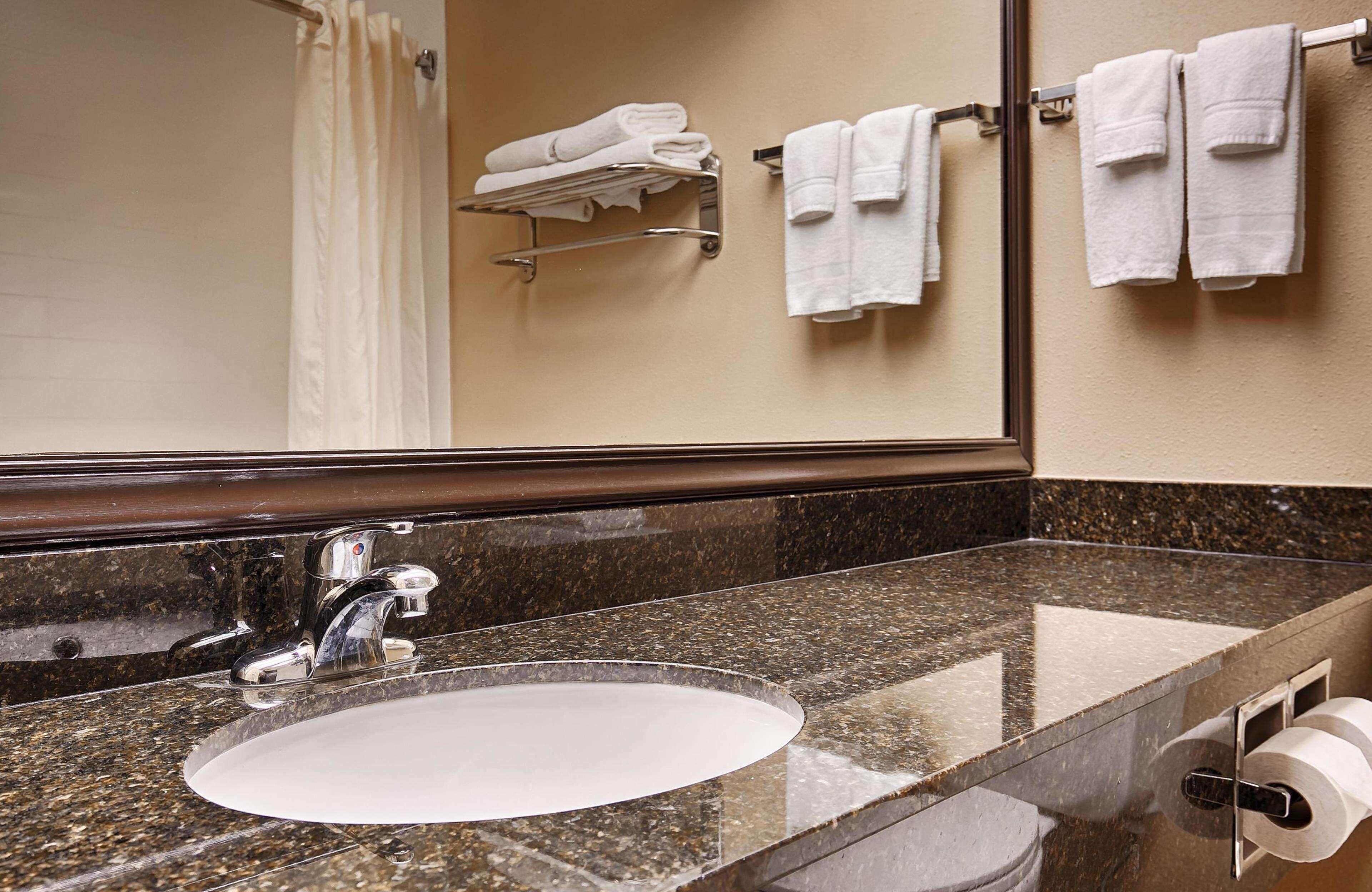 Une salle de bain avec un comptoir en granit, un lavabo, un miroir et un porte-serviettes sur lequel sont pliées des serviettes.