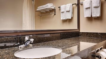 Une salle de bain avec un comptoir en granit, un lavabo, un miroir et un porte-serviettes sur lequel sont pliées des serviettes.