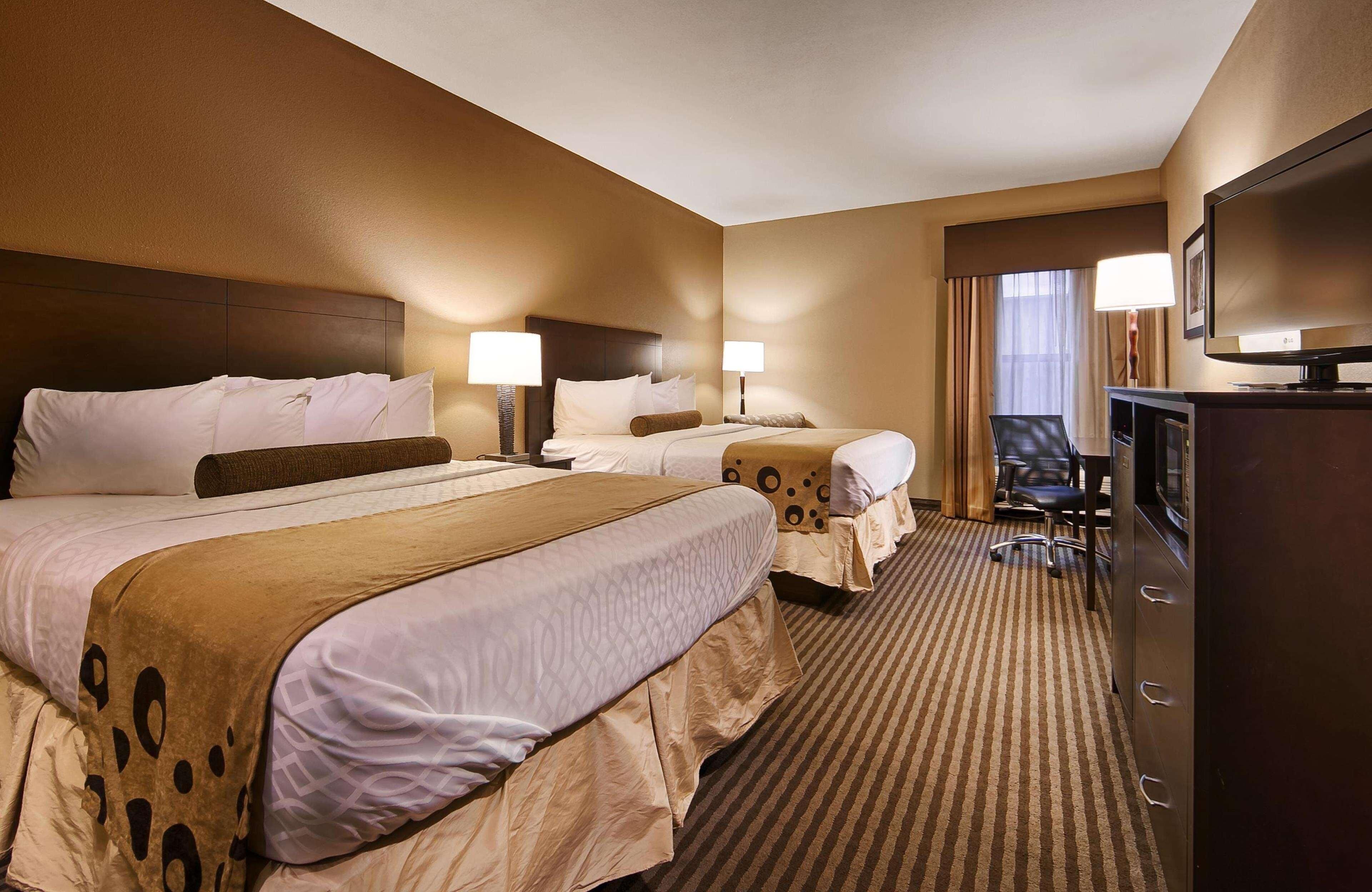 A hotel room with two beds, a television, a desk, and a chair.
