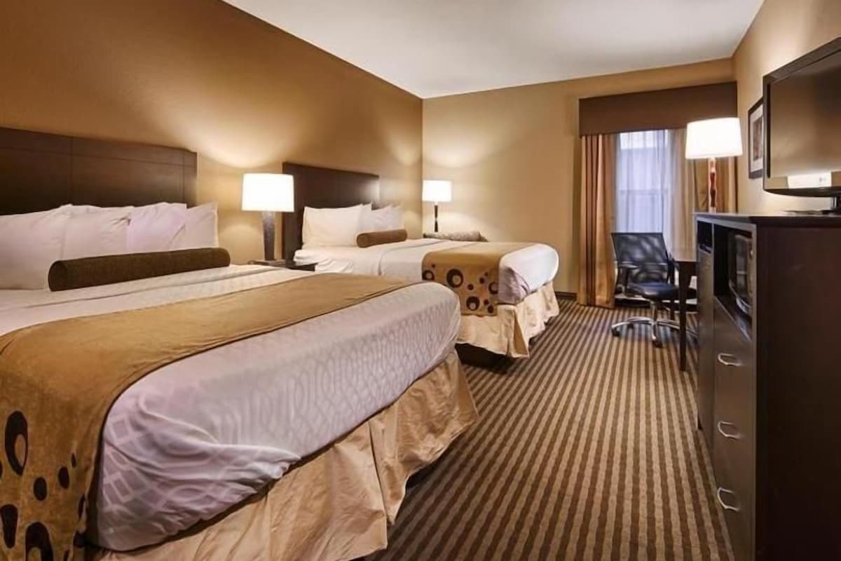 A hotel room with two beds, a television, a desk, and a chair.