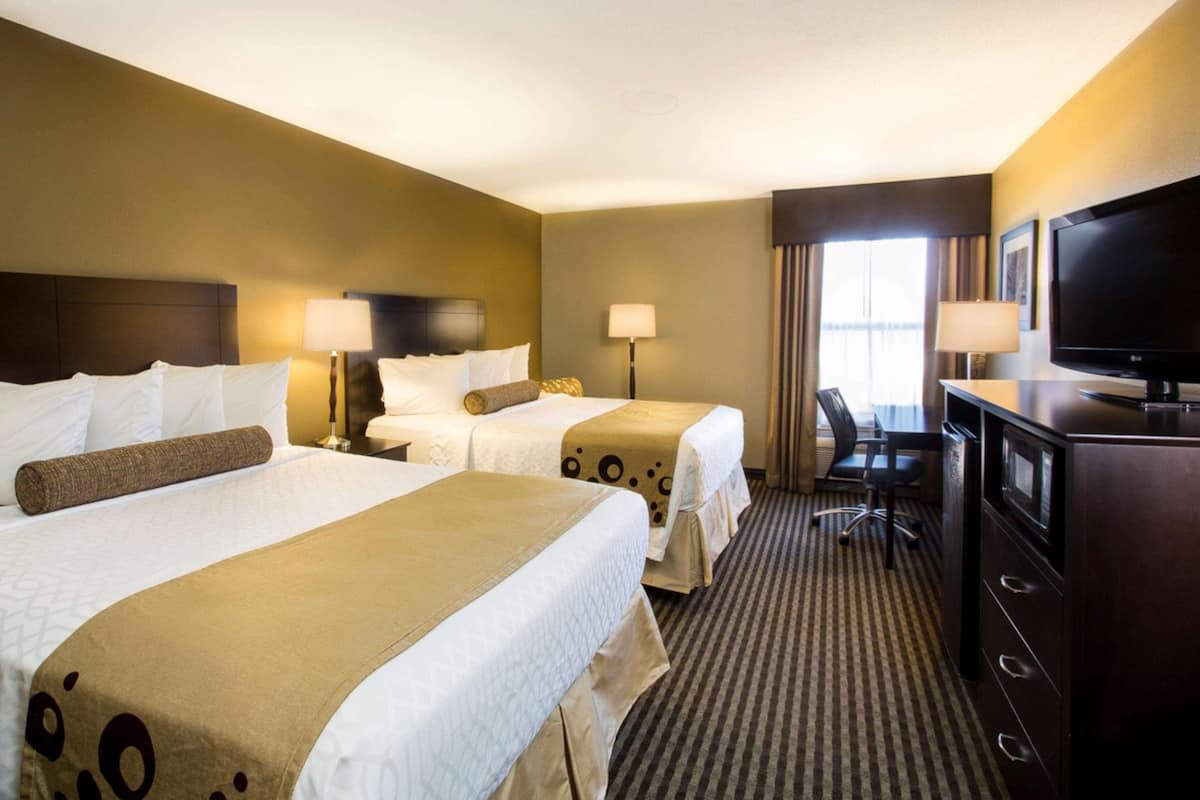 A hotel room with two beds, a desk, a television, and a window with curtains.