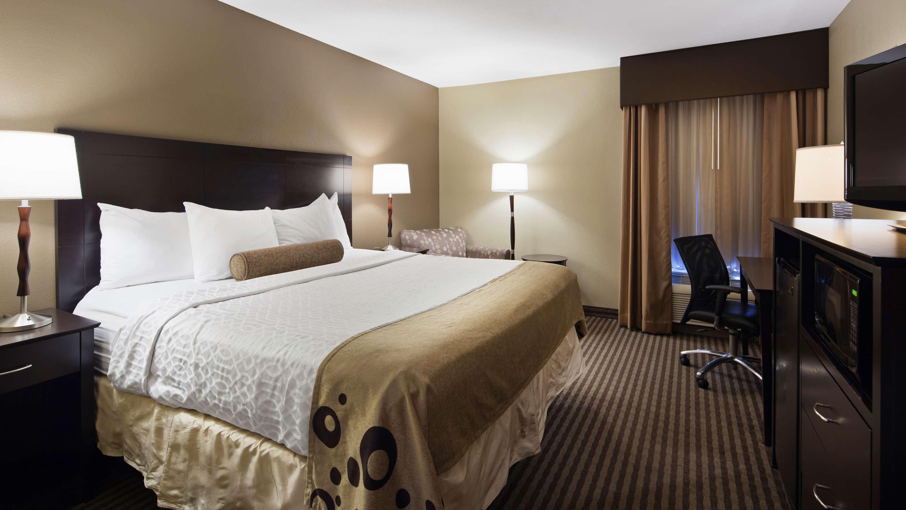 A hotel room with a large bed, two bedside tables with lamps, a desk with a chair, a television, and a minibar.