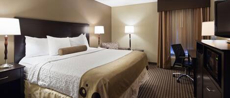 A hotel room with a large bed, two bedside tables with lamps, a desk with a chair, a television, and a minibar.