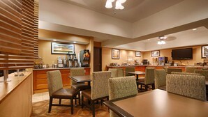 A hotel dining area with tables, chairs, a kitchen, and a television. - Mishawaka Inn (Mishawaka)
