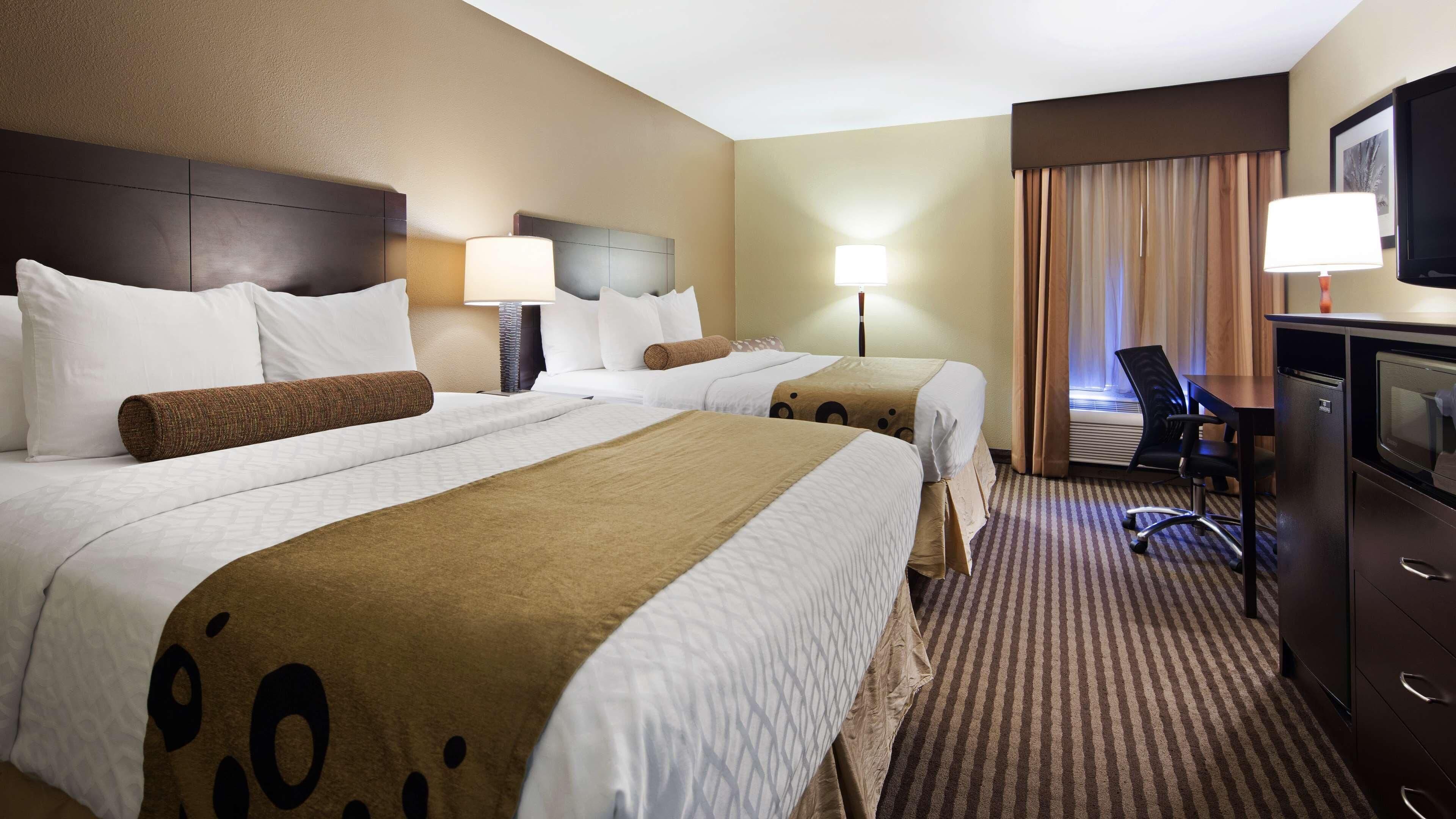 Ein Hotelzimmer mit zwei Betten, einem Schreibtisch, einem Sessel, einem Fernseher und einem Fenster mit Vorhängen.