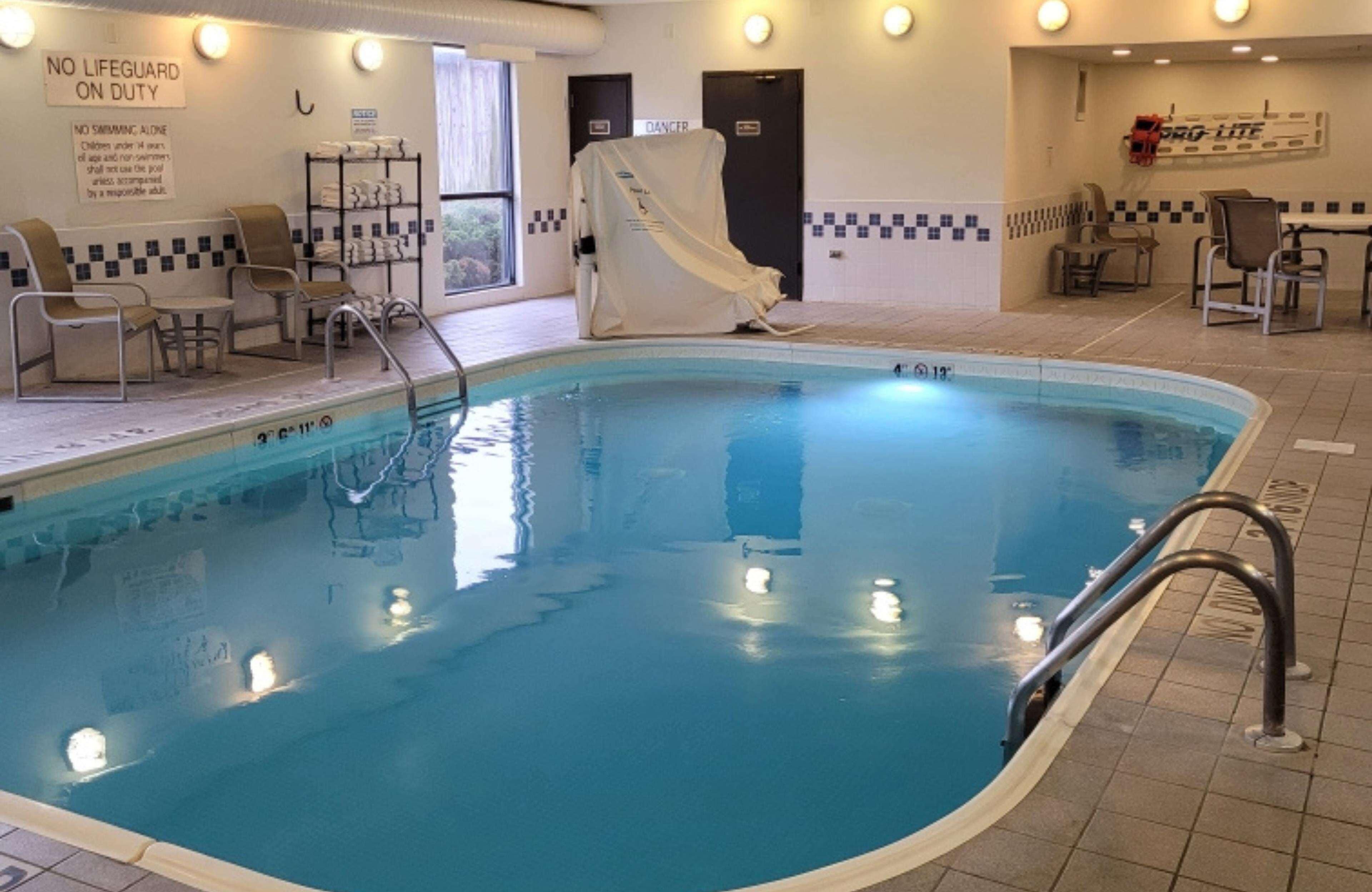A swimming pool with a no lifeguard on duty sign, a covered chair, and a poolside seating area.