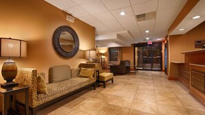 A lobby with a sofa, chairs, a lamp, a mirror, and a reception desk. - Mishawaka Inn (Mishawaka)