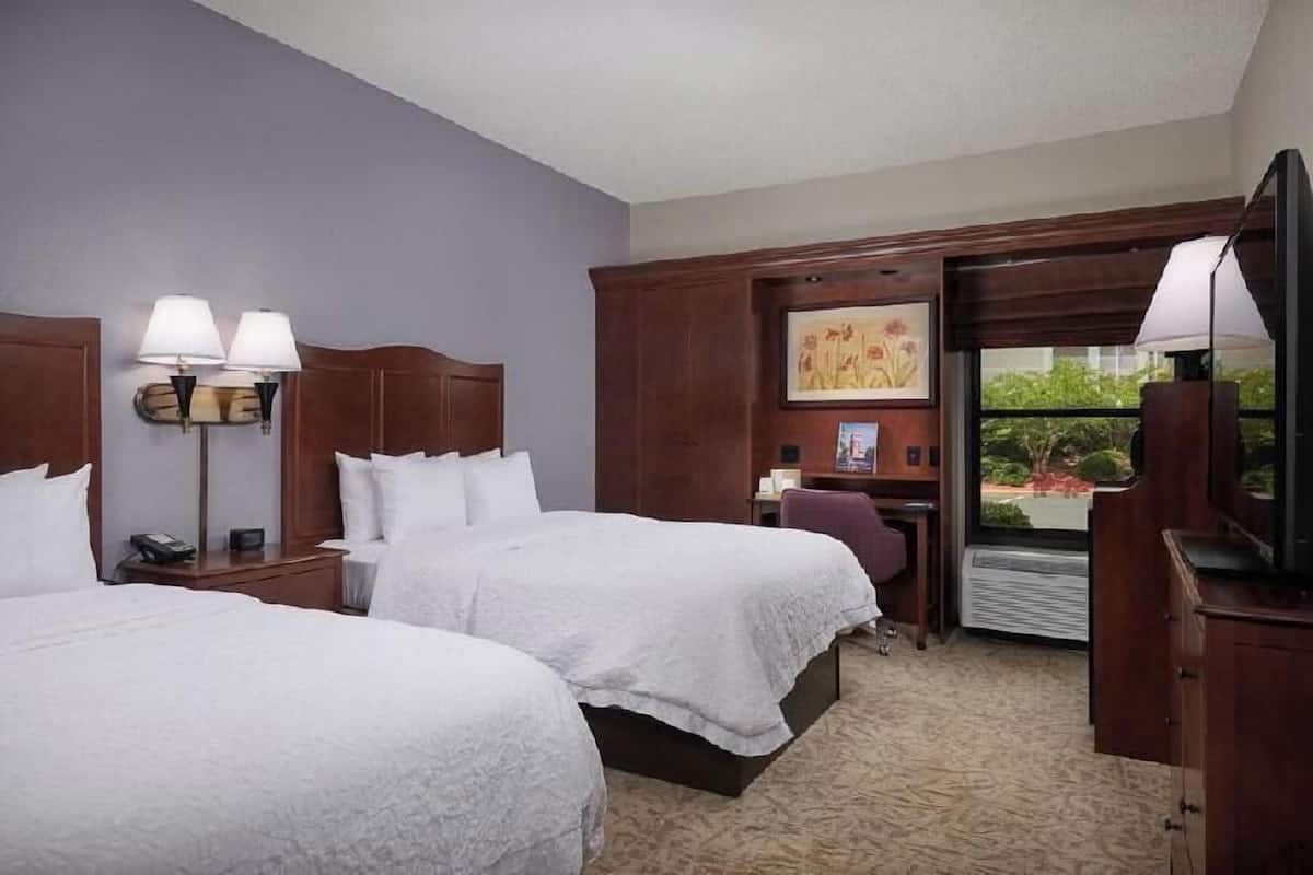 A hotel room with two beds, a desk, a chair, a television, and a window with a view.