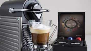 A Nespresso coffee machine with a glass cup of coffee and a pod holder.