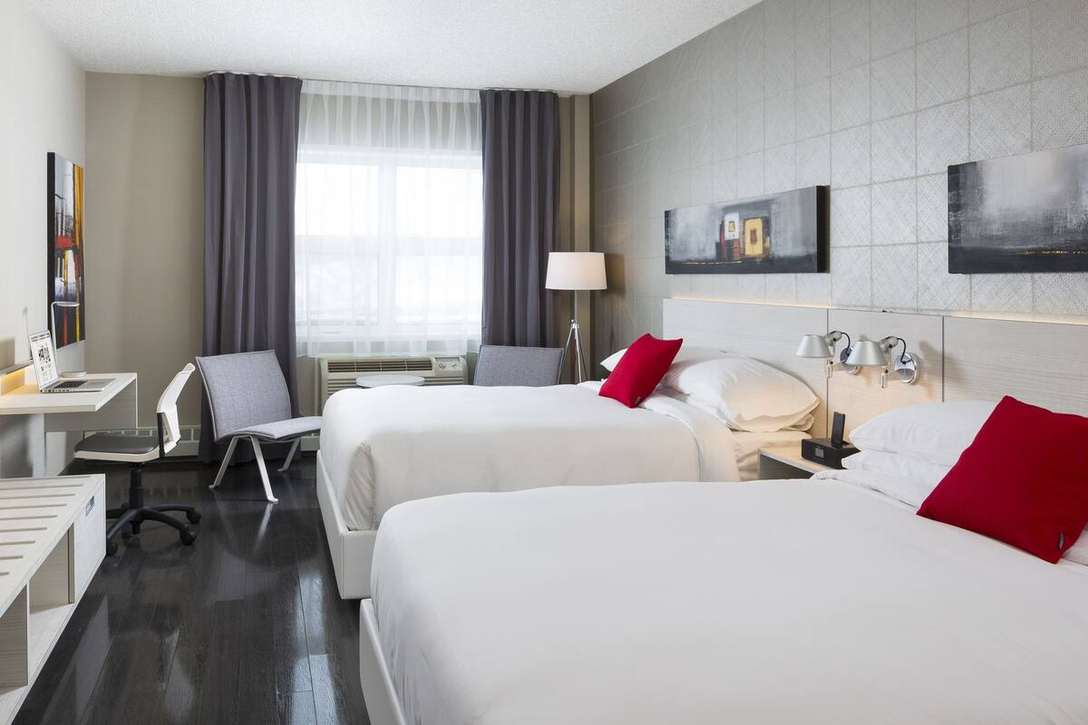 Habitación de hotel con dos camas, un escritorio con una computadora portátil, una silla, un televisor y una ventana con cortinas.