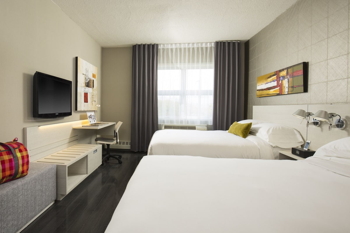Habitación de hotel con dos camas, un escritorio, televisión de pantalla plana y ventana con cortinas.