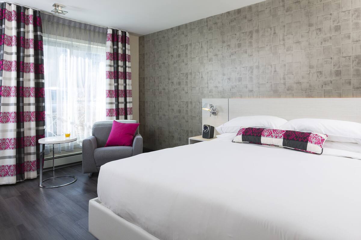 Una habitación de hotel con una cama grande, una mesita de noche, una silla y una ventana con cortinas.