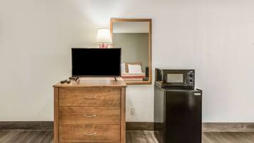 A hotel room with a wooden dresser, a flat-screen TV, a microwave, and a refrigerator.