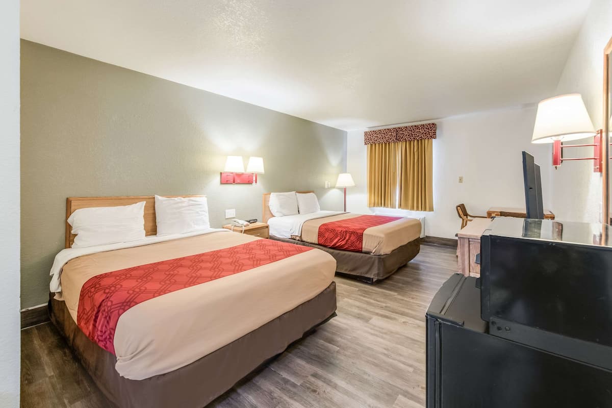 A hotel room with two beds, a TV, and a desk.