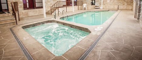 Una piscina interior con zona de jacuzzi, paredes de piedra y una escalera que conduce a una puerta.