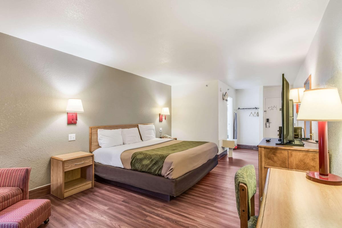 A hotel room with a bed, bedside tables, a chair, a desk, and a mirror.