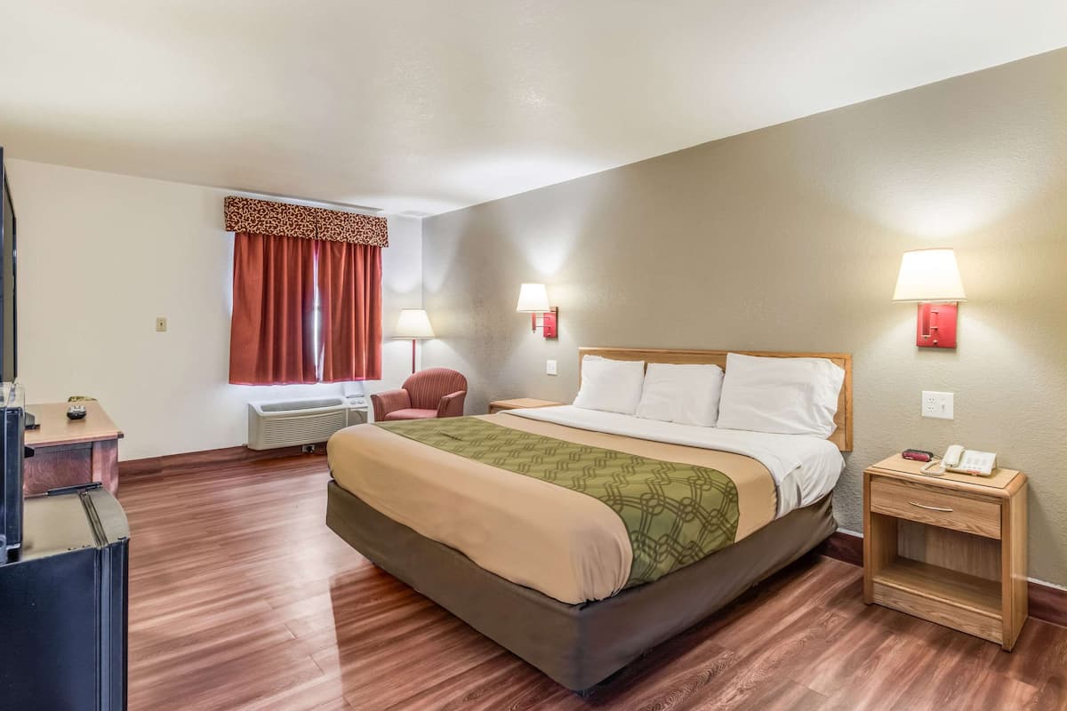 A hotel room with a large bed, two bedside lamps, a wooden nightstand, a desk, and a chair.