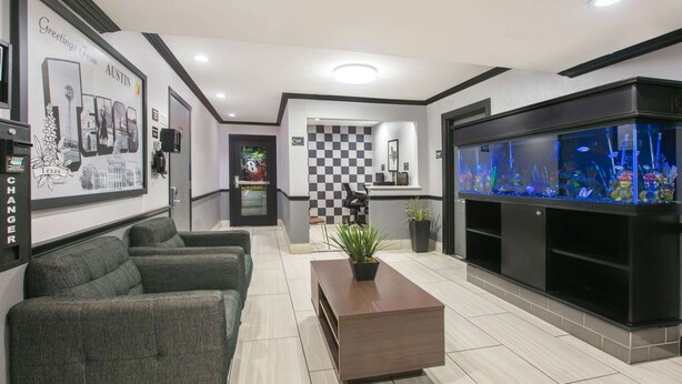 A hotel lobby with a reception desk, a checkered wall, a large aquarium, and two sofas. - Super 8 by Wyndham Austin University/Downtown Area (Austin)