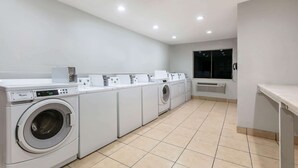 A laundry room with multiple washing machines and dryers, a tiled floor, and a window with a view of the outside. - Super 8 by Wyndham Austin University/Downtown Area (Austin)