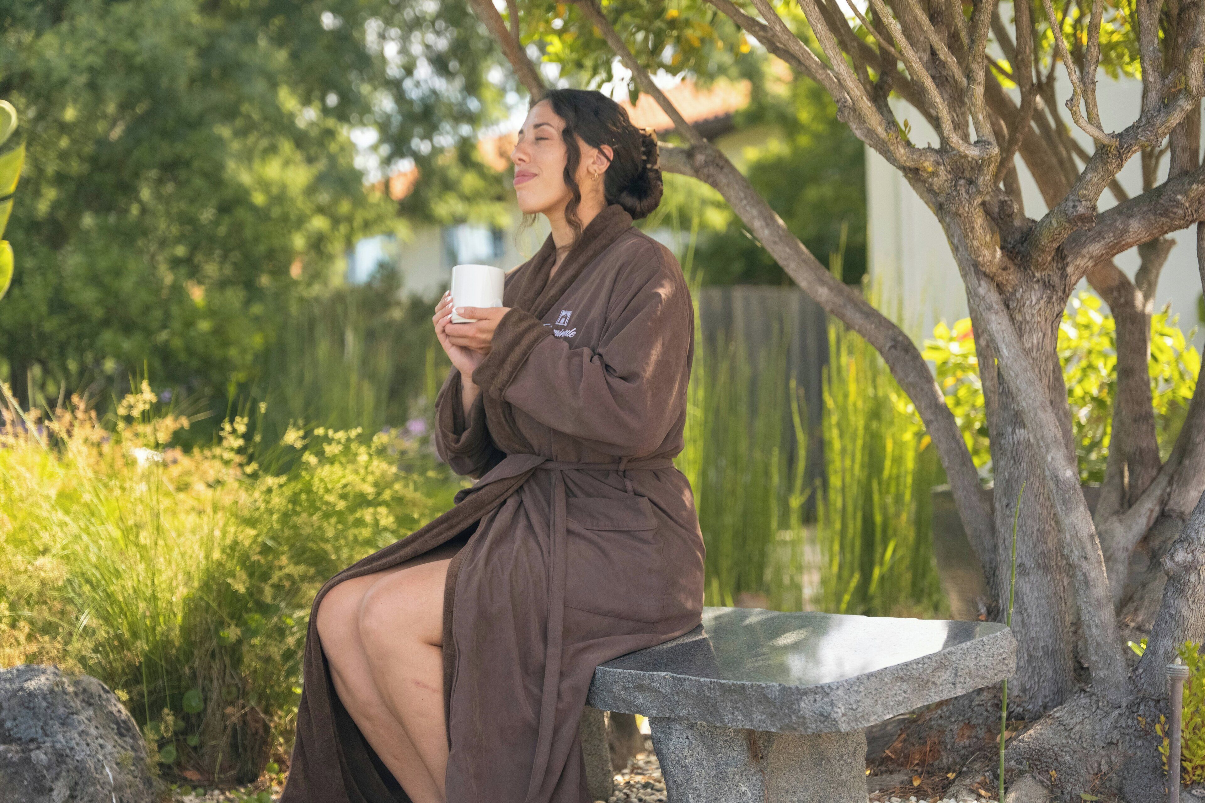 A person sitting on a stone bench outdoors, holding a white mug.
