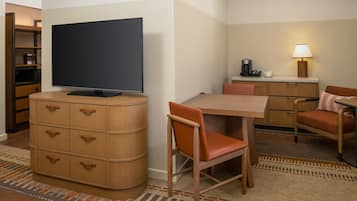 A hotel room with a television, a desk with a coffee maker, a chair, and a cabinet with drawers.