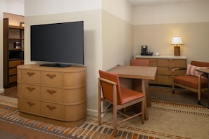 A hotel room with a television, a desk with a coffee maker, a chair, and a cabinet with drawers.