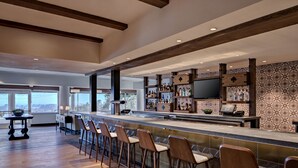A modern bar area with wooden bar stools, a counter with a television, and shelves stocked with bottles. - Chaminade Resort & Spa (Santa Cruz)