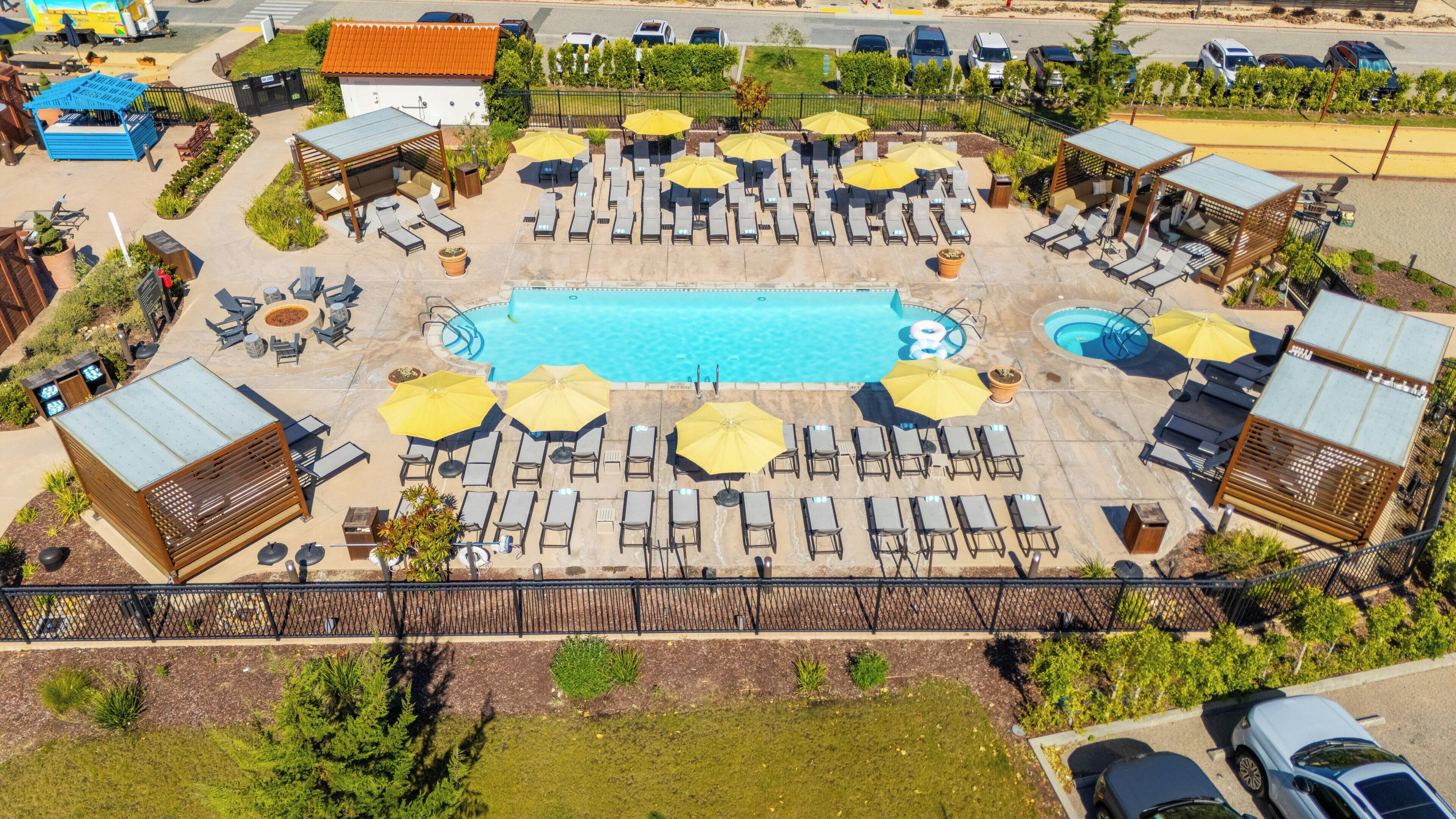 A rooftop pool area with multiple sun loungers and umbrellas, surrounded by a fence and various buildings.