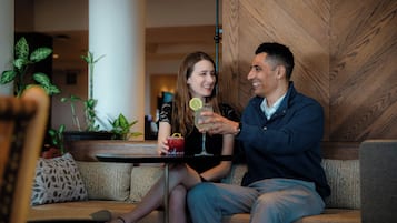 A man and a woman sitting on a sofa with a table between them, holding drinks.