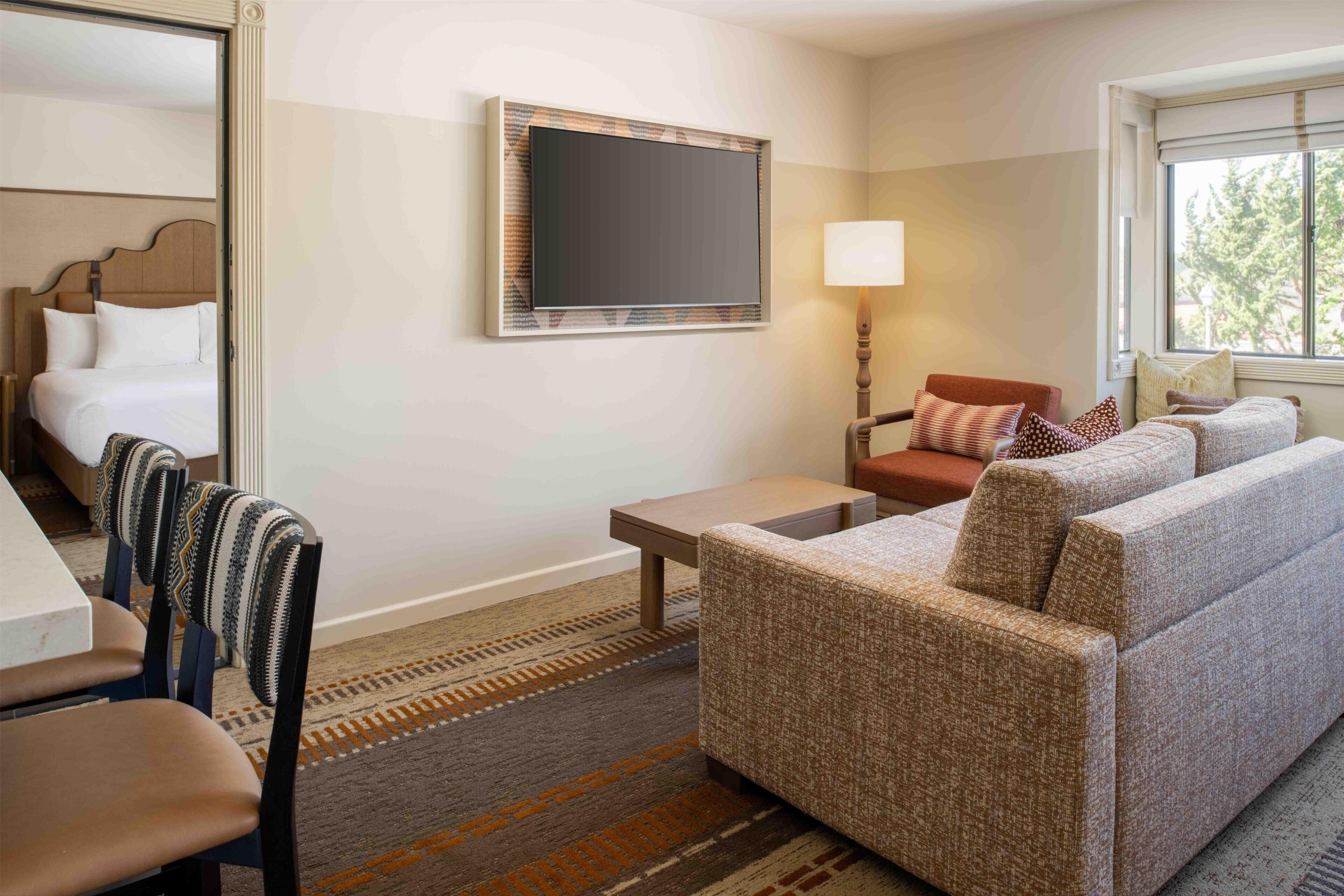A hotel room with a bed, a sofa, a TV, a lamp, and a window.