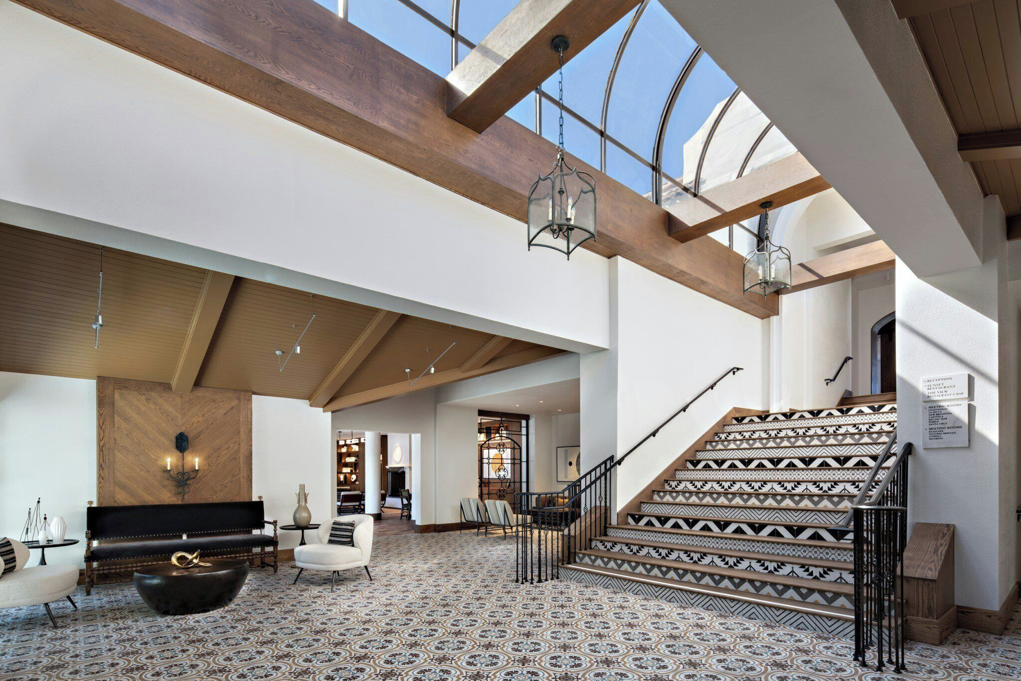 A spacious interior with a high ceiling, a staircase with patterned tiles, and a seating area with a fireplace.