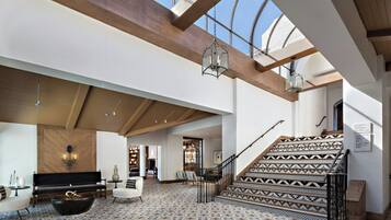 A spacious interior with a high ceiling, a staircase with patterned tiles, and a seating area with a fireplace.