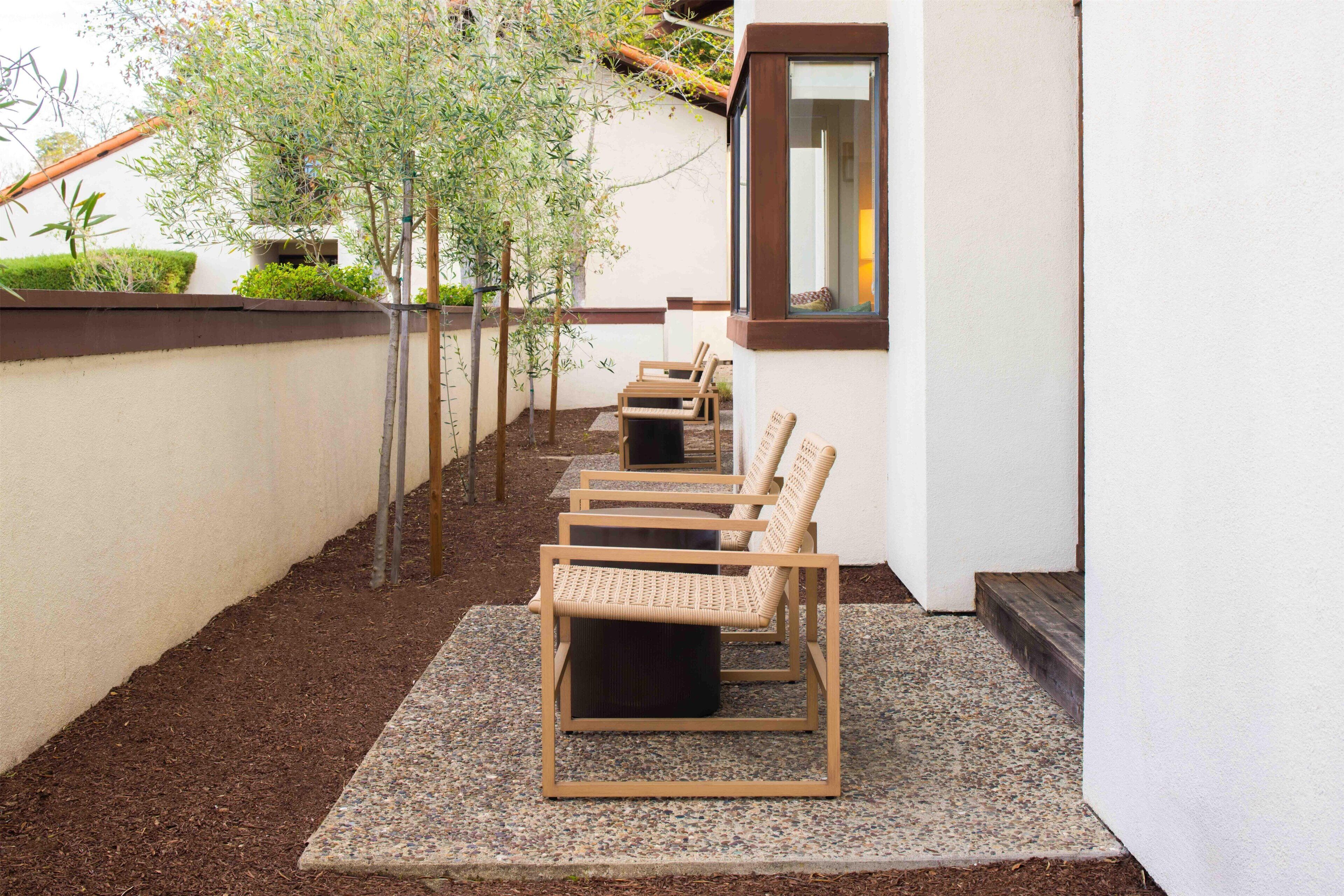A row of wicker chairs on a gravel patio adjacent to a building with a window.
