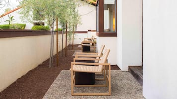 A row of wicker chairs on a gravel patio adjacent to a building with a window.