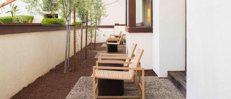 A row of wicker chairs on a gravel patio adjacent to a building with a window.
