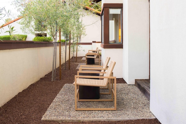 A row of wicker chairs on a gravel patio adjacent to a building with a window.