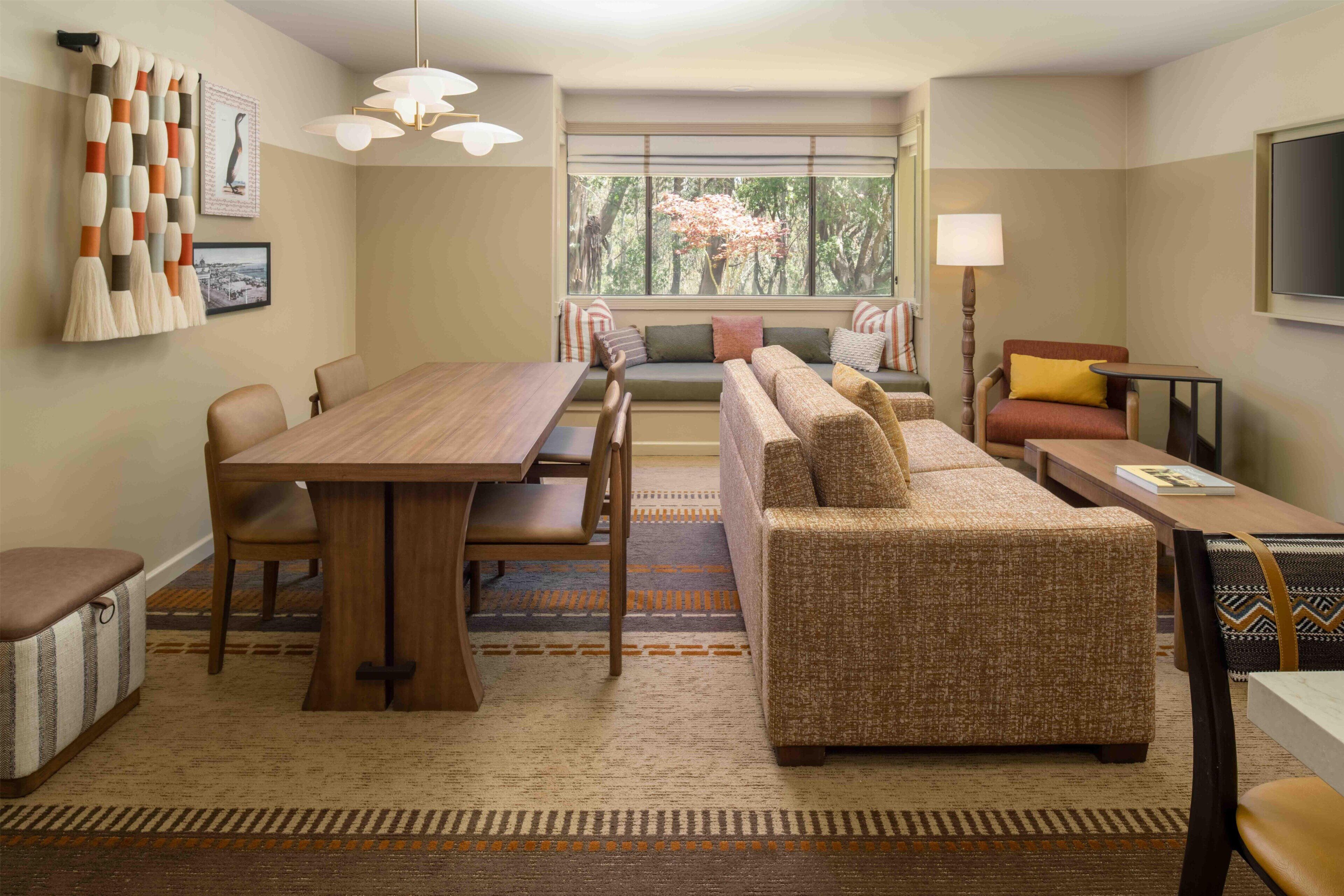 A modern living room with a dining table, sofa, and a large window with a view of trees.