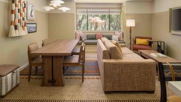 A modern living room with a dining table, sofa, and a large window with a view of trees.