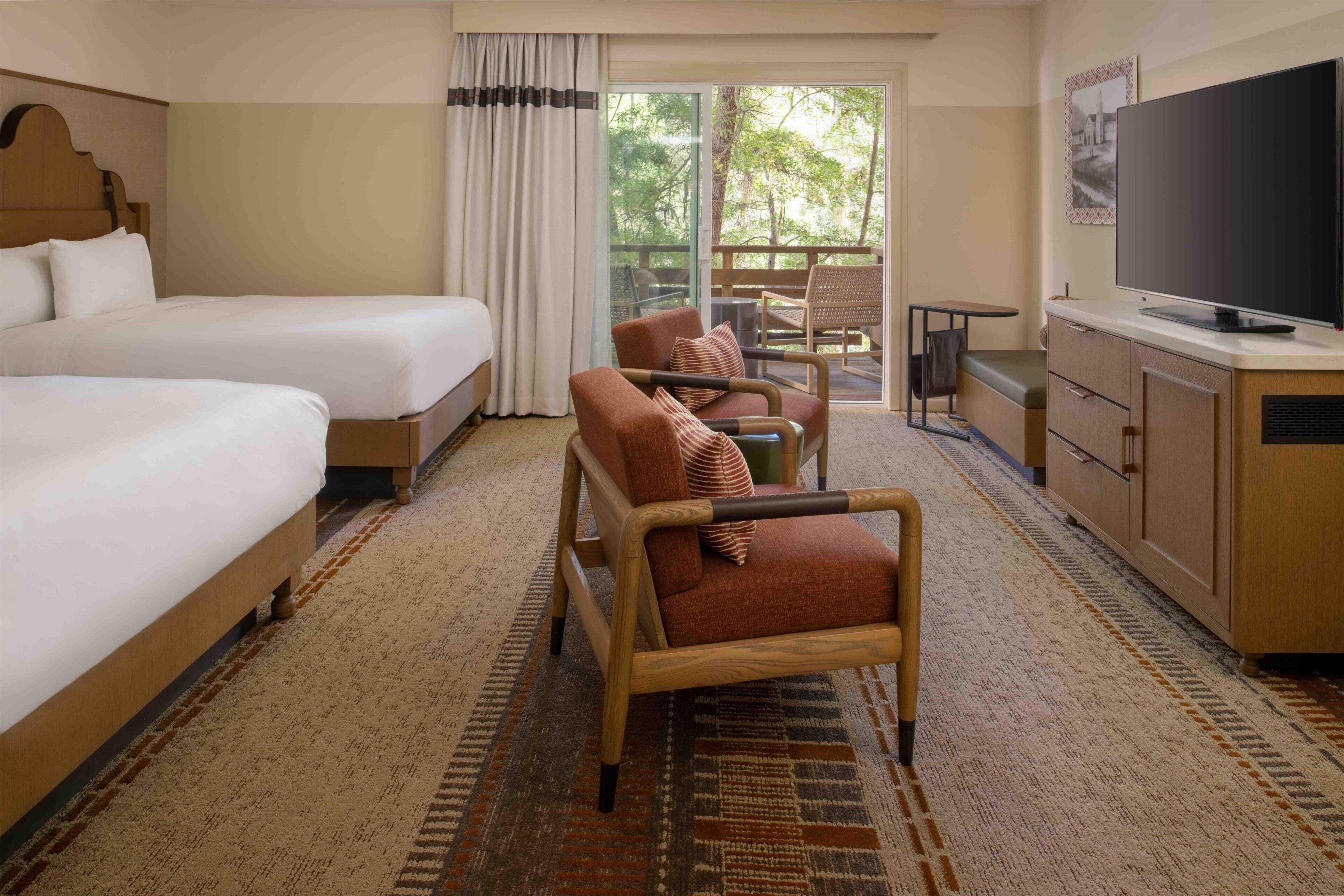 Quarto de hotel com duas camas, um sofá, uma televisão e vista para o exterior.