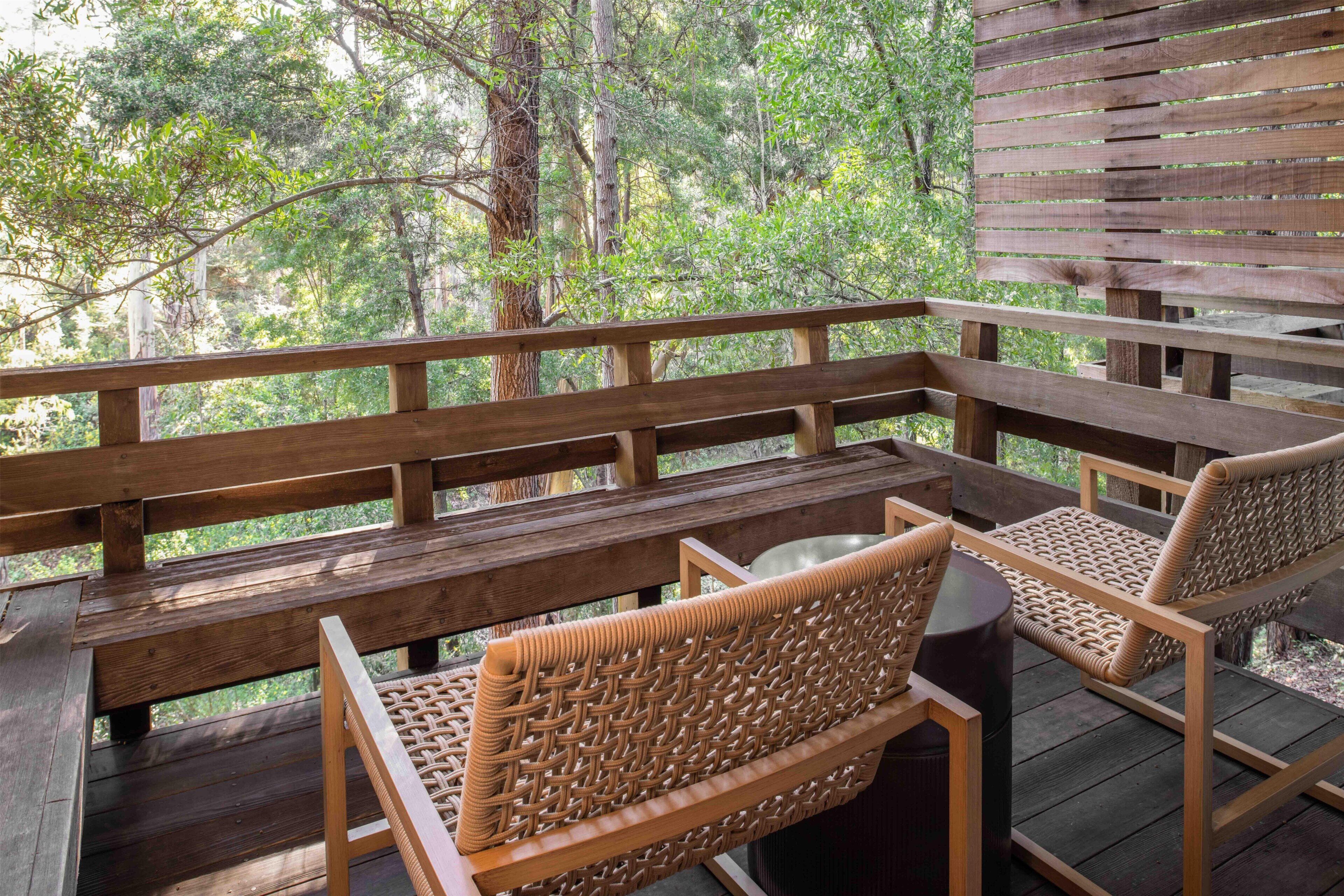 A wooden deck with a bench and wicker chairs, overlooking a forested area.