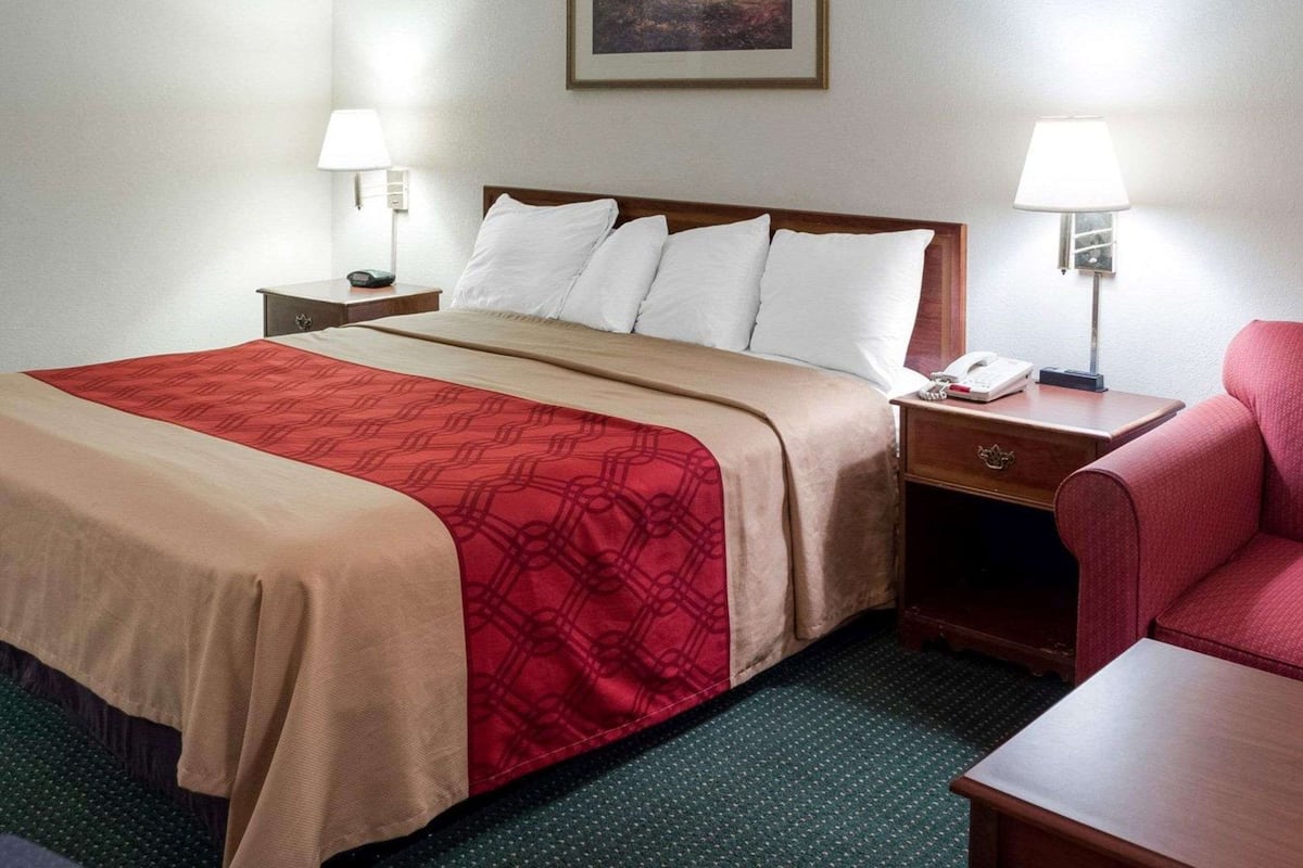 A hotel room with a bed, two bedside tables, a chair, and a painting on the wall.