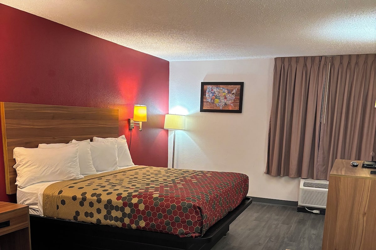 A hotel room with a bed, bedside lamps, a desk, and a wall-mounted air conditioner.