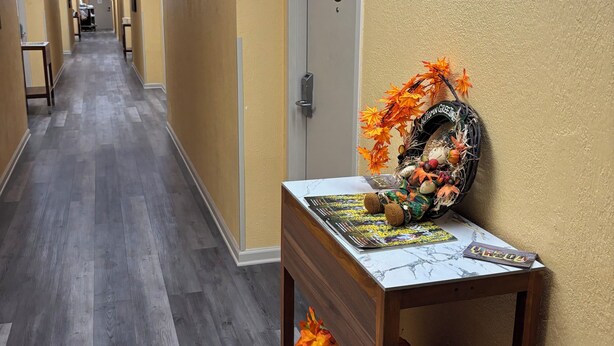 Un pasillo de hotel con suelo de madera, una recepción decorada con motivos otoñales y una puerta con el número 104.