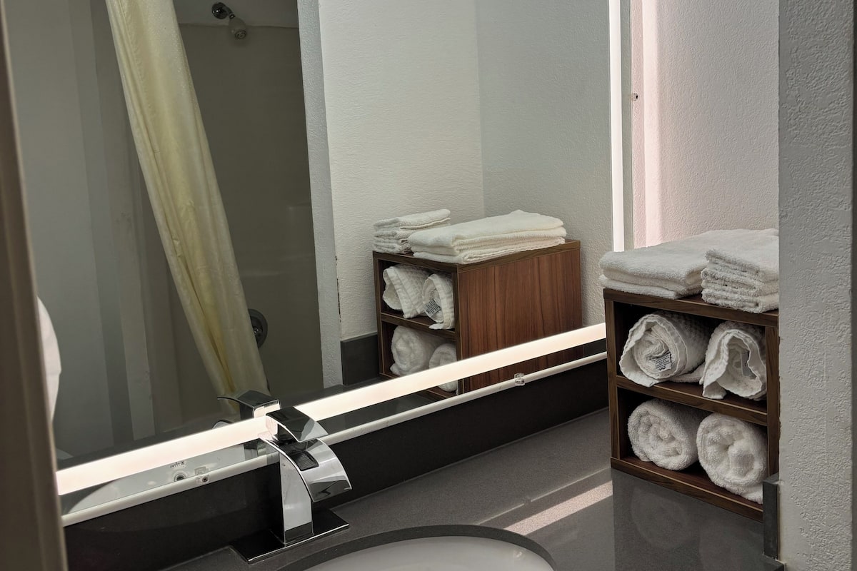 A bathroom with a large mirror, a sink, and shelves with neatly folded towels.