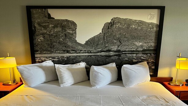 Una habitación de hotel con una cama grande, ropa de cama blanca y una fotografía enmarcada de un paisaje en la pared.