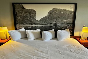 Una habitación de hotel con una cama grande, ropa de cama blanca y una fotografía enmarcada de un paisaje en la pared.