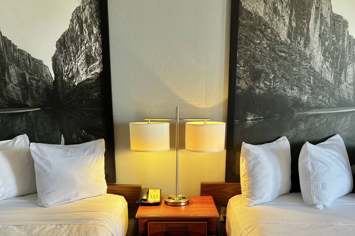 Une chambre d’hôtel avec deux lits, une table de chevet avec une lampe et un téléphone fixé au mur.