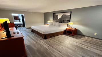 Habitación de hotel con una cama grande, un escritorio con lámpara, una mesita de noche y un cuadro en la pared.