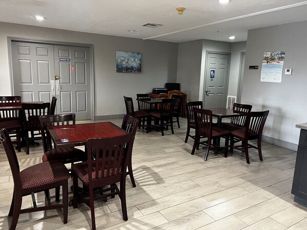 A dining area with wooden tables and chairs, a painting on the wall, and a door with a sign.